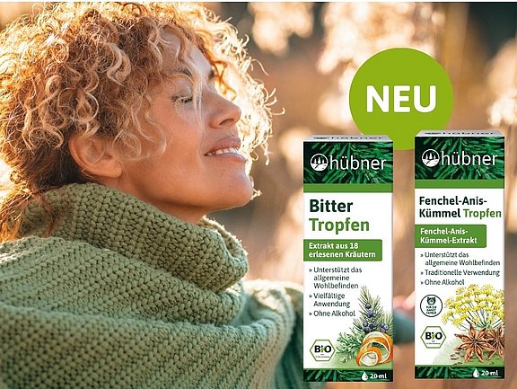 Eine Person mit lockigem Haar lächelt, hat geschlossene Augen und trägt ein grünes Kopftuch. Im Vordergrund stehen zwei Schachteln mit Kräutertropfen. Oben rechts ist ein grüner Kreis mit „NEU“ zu sehen, der auf neue Produkte hinweist. Der Hintergrund ist sonnenbeschienen und grün.