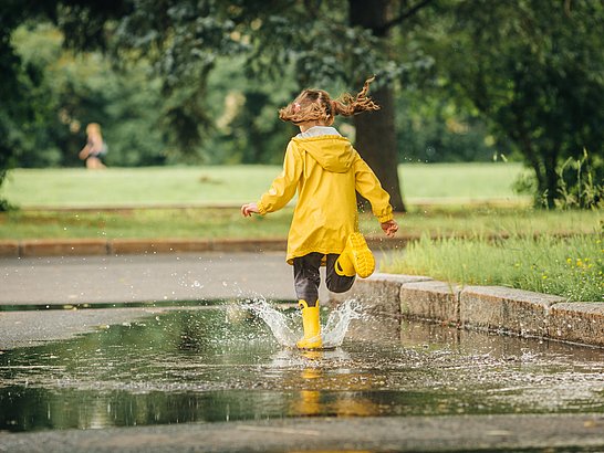 Ratgeber Immunsystem Stärken Kind mit gelber Regenjacke springt in Pfütze